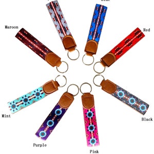 May include: Ten colorful keychains with different geometric patterns and a brown leather strap. The keychains are arranged in a circle with the key rings facing inwards. The colors of the keychains are gray, blue, maroon, red, mint, purple, pink, and black.