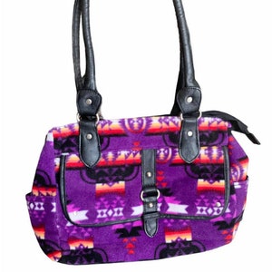 May include: A purple handbag with a Southwestern-inspired pattern in shades of red, orange, and black. The bag has black leather handles, trim, and a buckle closure. It features two front pockets and a zipper closure.