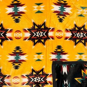 Könnte beinhalten: Eine gelbe Fleece-Decke mit einem geometrischen Muster in Schwarz, Weiß, Rot und Grün. Die Decke hat ein Design im Südwest-Stil.