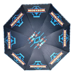 Puede incluir: Un paraguas negro con un diseño del suroeste. El paraguas presenta patrones geométricos en tonos de azul, naranja, rojo y blanco. El diseño se repite en la superficie del paraguas, creando un patrón simétrico.