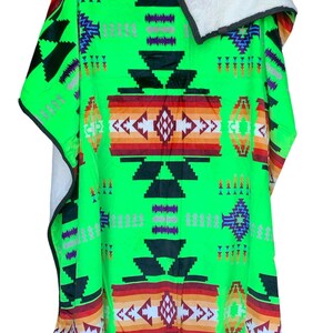 May include: A green fleece throw blanket with a Southwestern-style geometric pattern in shades of red, orange, white, black, and purple. The blanket has a soft, plush texture and is reversible with a white sherpa lining.