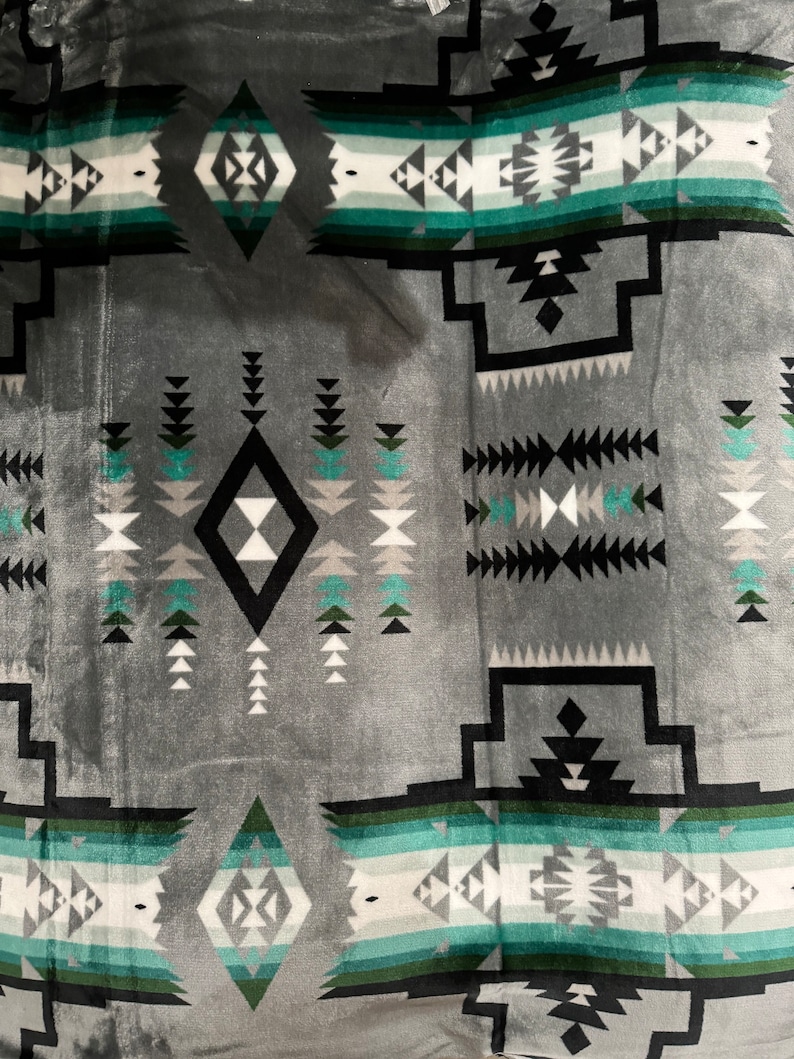 May include: Gray and teal patterned throw blanket with a geometric design. The blanket features a diamond shape in the center with a black outline and a white interior.