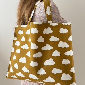 Peut inclure: Sac fourre-tout moutarde avec un motif de nuages blancs répétés. Le sac a deux anses et est fait d'un tissu robuste. Le design est simple et fantaisiste, adapté au transport de courses ou d'objets personnels.
