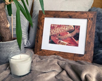 May include: A framed photograph of a woman's hand and foot adorned with intricate gold jewelry. The jewelry features a delicate anklet and several bracelets. The woman is wearing a red and gold garment.