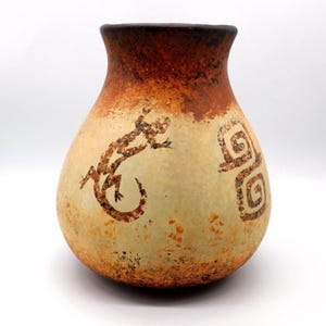 May include: A rounded ceramic vase with a wide base and narrow neck, featuring a cream-colored body with mottled orange-brown gradients at the top and bottom. The surface is decorated with a dark brown lizard silhouette and a spiral pattern.