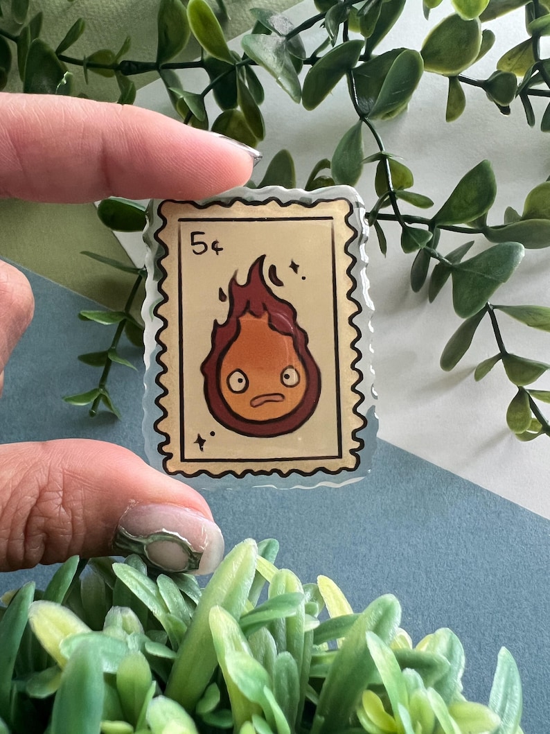 May include: A clear, rectangular sticker resembling a postage stamp, featuring a cartoon fire demon with a surprised expression. The stamp reads "5&cent;" in the upper left corner. The fire demon is red and orange with a brown outline.