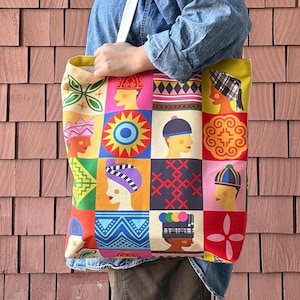 May include: A colorful tote bag with a repeating pattern of stylized faces wearing various hats. The bag features a yellow interior and white straps. The design includes vibrant colors like pink, orange, blue, and green.