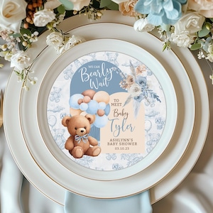 May include: A blue and white baby shower plate with a teddy bear holding balloons and the text "We can Bearly Wait to meet Baby Tyler, Ashlynn's Baby Shower 03.10.23"