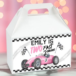 Pode incluir: Caixa de presente branca com um design de carro de corrida rosa e bandeira quadriculada. O texto na caixa diz "Emily is Two Fast 2 Curious".
