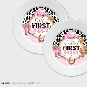 May include: Two white paper plates with a pink and brown design featuring a cowboy hat, boots, and a horseshoe. The text on the plates reads "Millie's First Rodeo".