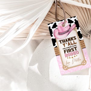 May include: Pink and brown thank you tag with a cow print background. The tag says "Thanks Y'all for coming to my First Rodeo" with a pink cowboy hat and stars. The tag is tied with a brown string.
