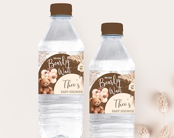 Peut inclure: Deux bouteilles d'eau en plastique transparent avec des étiquettes brunes. Les étiquettes représentent un ours en peluche de dessin animé avec des ballons et le texte "We can Bearly Wait Theo's Baby Shower".