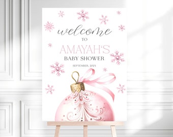 May include: Pink and gold welcome sign for a baby shower with the text "Welcome to Amayah's Baby Shower, September, 2023". The sign features a pink and gold Christmas ornament with snowflakes.