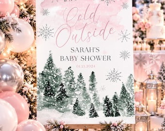 May include: A rectangular sign on a wooden easel featuring a pink watercolor wash background, silver snowflake illustrations, and a forest of green pine trees. The text reads: BABY IT'S Cold Outside, SARAH'S BABY SHOWER, and the date 01.21.2024.