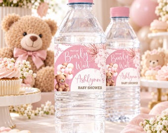 May include: Two clear plastic water bottles with pink caps and custom labels featuring a brown teddy bear, pink balloons, and the text "We Can Bearly Wait" and "Ashlynn's Baby Shower" in a decorative script and sans-serif font style.