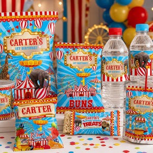 K&ouml;nnte beinhalten: Eine Sammlung von Partyartikeln mit Zirkus-Thema, darunter Snackbeutel, Wasserflaschen und Saftbeutel. Die Produkte zeigen den Text "Carter's 1st Birthday" und Illustrationen von Zirkustieren und -zelten.