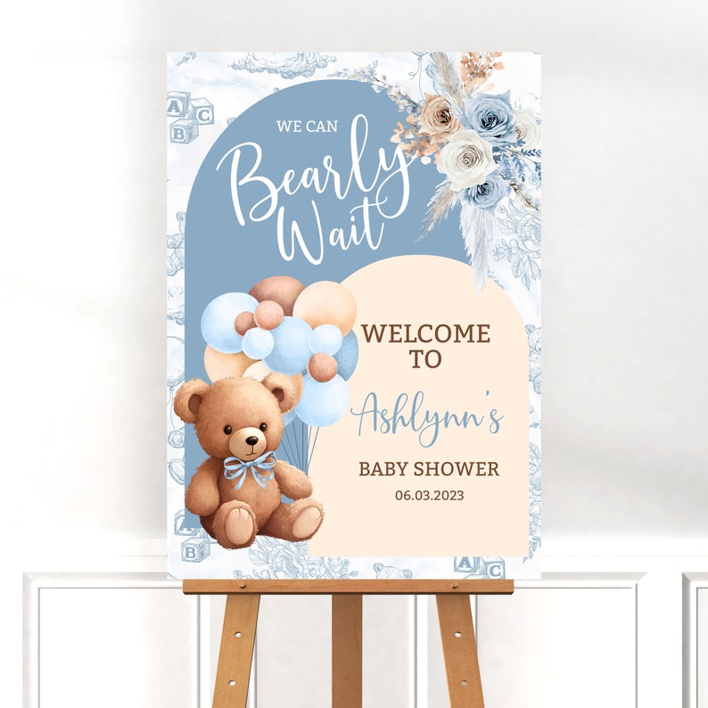 May include: A blue and beige baby shower welcome sign with the text "We can Bearly Wait" and "Welcome to Ashlynn's Baby Shower 06.03.2023". The sign features a teddy bear holding blue and brown balloons.