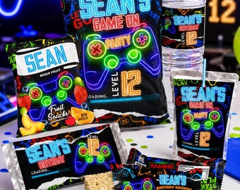 May include: A collection of custom party favors featuring a neon gaming theme with the text Sean's Game On, Sean's Birthday, and Level 12. The set includes a snack bag, a water bottle, a juice pouch, a candy bar wrapper, and a rice cereal treat.