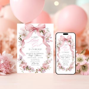 May include: A baby shower invitation and a smartphone showing the same design. The invitation and phone screen display a floral wreath with a pink bow and the text "A Sweet Little Girl Is On Her Way!" The invitation includes event details.