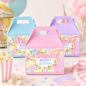 May include: Three colorful carnival-themed favor boxes in pink, blue, and purple. Each box features a handle and a label with carnival graphics, including a Ferris wheel, popcorn, and the text "Maddie's Carnival". Confetti and popcorn are scattered around.