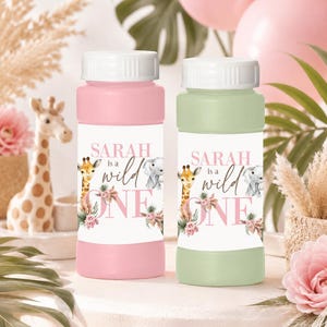 May include: Two cylindrical bubble solution bottles with white screw-on caps. One bottle is pink, the other is light green. Each features a label with the text 'SARAH is a wild ONE' alongside watercolor illustrations of a giraffe, elephant, and flowers.