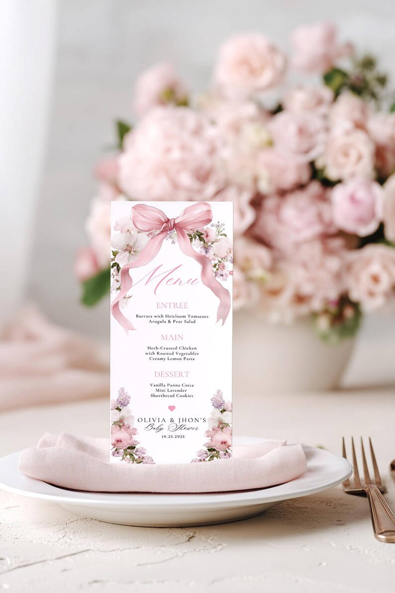 May include: A baby shower menu card featuring a pink bow and floral decorations. The menu lists entree, main, and dessert choices. The card rests on a white plate with a pink napkin, with a bouquet of pink flowers in the background.