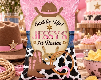 以下が含まれることがあります： 上部にピンクのペイズリー柄、中央の楕円形に「Saddle Up! JESSY'S 1st Rodeo」の文字、下部に白黒の牛柄があしらわれた長方形のスナック袋。デザインには茶色のカウボーイハット、ブーツ、投げ縄が含まれています。