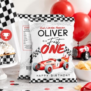May include: A white snack bag with a black and white checkered border, featuring a red race car illustration, checkered flags, and the text "Our Little Racer OLIVER IS A Fast ONE HAPPY BIRTHDAY" with a nutrition label graphic on the side.