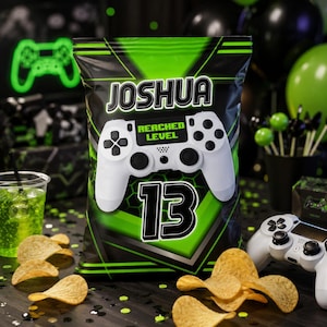 May include: A rectangular snack bag with a black and green geometric background featuring the name JOSHUA at the top, a white video game controller graphic in the center with the text REACHED LEVEL, and the large number 13 printed below it.