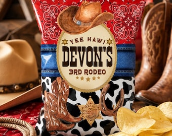 Op de afbeelding: Een zak Devon's 3rd Rodeo chips met een cowboythema. De zak heeft een bruine cowboyhoed, denim-stijl accenten en een zwart-wit koeienhuidpatroon. De tekst "Yee Haw!" en "Grand Sheriff County" zijn ook zichtbaar.