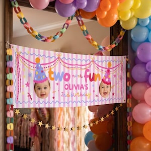 Puede incluir: Una pancarta de cumpleaños rectangular con rayas verticales rosas y blancas, con el texto "two much fun" y "OLIVIA'S 2nd birthday". La pancarta muestra dos fotos de un niño con un gorro de fiesta, decorada con cadenas de papel y globos.