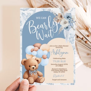 May include: A blue and brown baby shower invitation with a teddy bear holding balloons. The invitation says "We can Bearly Wait" and includes the name Ashlynn and the baby's name Tyler Blue. The invitation also includes the date, time, and location of the shower. It says "Registered at Target and Amazon".