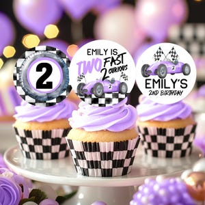 May include: Three purple and white cupcake toppers with a checkered pattern. The toppers feature a purple race car with the text "Emily is Two Fast 2 Curious" and "Emily's 2nd Birthday".