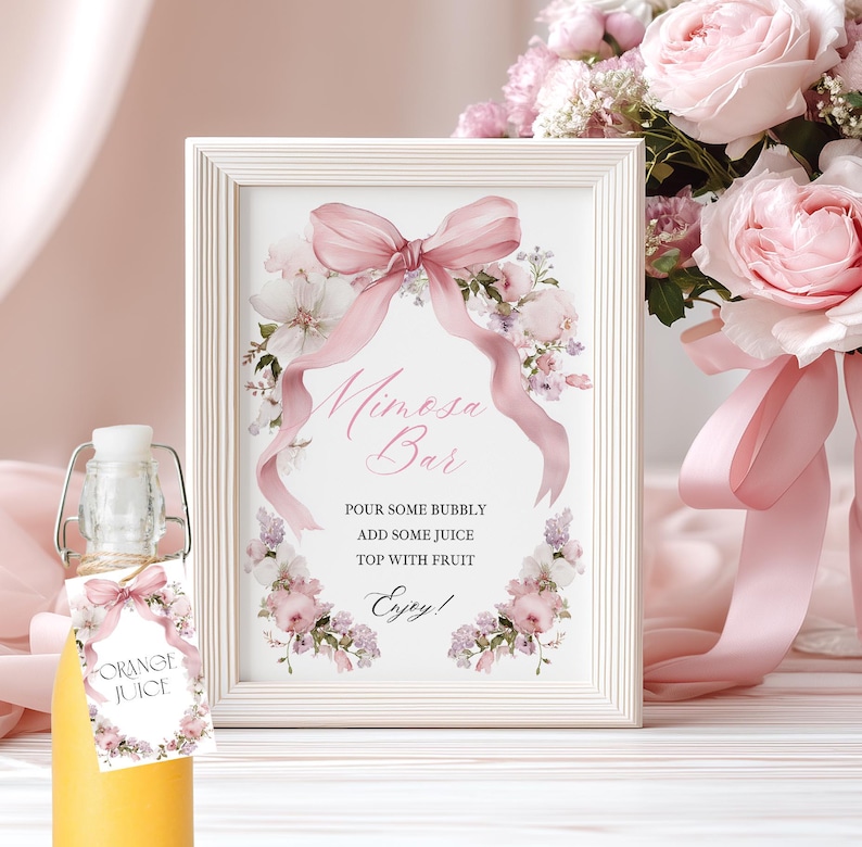 May include: A white framed sign reading "Mimosa Bar" with a pink bow and floral decorations. A bottle of orange juice with a floral tag is in front. The sign says: "Pour some bubbly, add some juice, top with fruit, enjoy!"