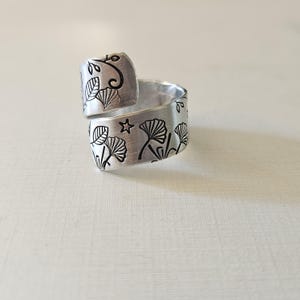 Può includere: Un anello regolabile in argento con un design di foglie di ginkgo e una stella. L'anello è in metallo e ha una finitura martellata.
