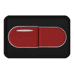 May include: A red embroidered patch in the shape of a pill on a black background.