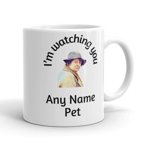 May include: White ceramic mug with a handle. The mug features an image of a woman in a hat, with the text "I'm watching you" arched above the image. Below the image, the text reads "Any Name Pet".