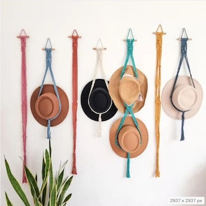 May include: Seven macrame wall hangings with tassels, each holding a different colored hat. The hats are brown, beige, black, and turquoise.