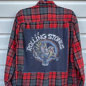 May include: Red, black, and gray plaid flannel shirt with a large navy blue patch on the back. The patch features the words "Rolling Stones" around a graphic of a winged creature.