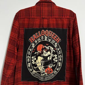 May include: Red and black plaid flannel shirt with a large black patch on the back. The patch features the text "HALLOQUEEN" in an oval design with a spooky illustration and the words "MURDER APPAREL".