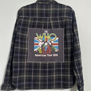 May include: A long-sleeved, button-down flannel shirt in a dark blue, green, and tan plaid pattern. The back features a gray patch with "The Who" logo, the Union Jack, and the text "American Tour 1976".