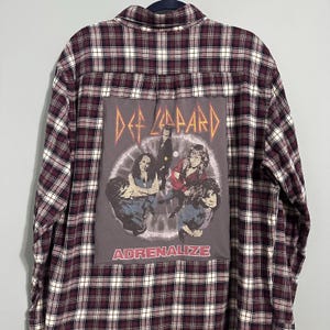 May include: A maroon and black plaid flannel shirt with a Def Leppard graphic on the back. The graphic features the band's name in orange and a picture of the band members with the word "ADRENALIZE" below.
