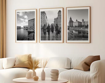 May include: Three vertical black and white framed wall art prints displayed in a row. The left print shows a waterfront building, the center print depicts four people walking on a city street, and the right print features a large historic building.