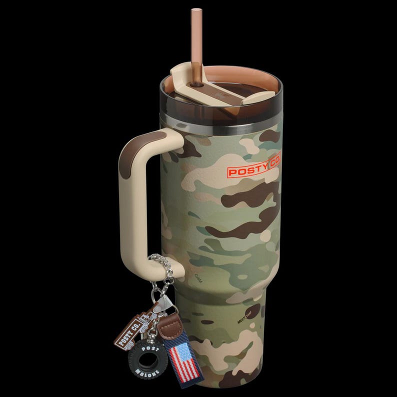May include: A camouflage-patterned tumbler with a handle, straw, and lid. The tumbler has the text "POSTY CO." in red. A keychain with a tire-shaped charm, a blue and red striped tag, and a leather tag is attached to the handle.