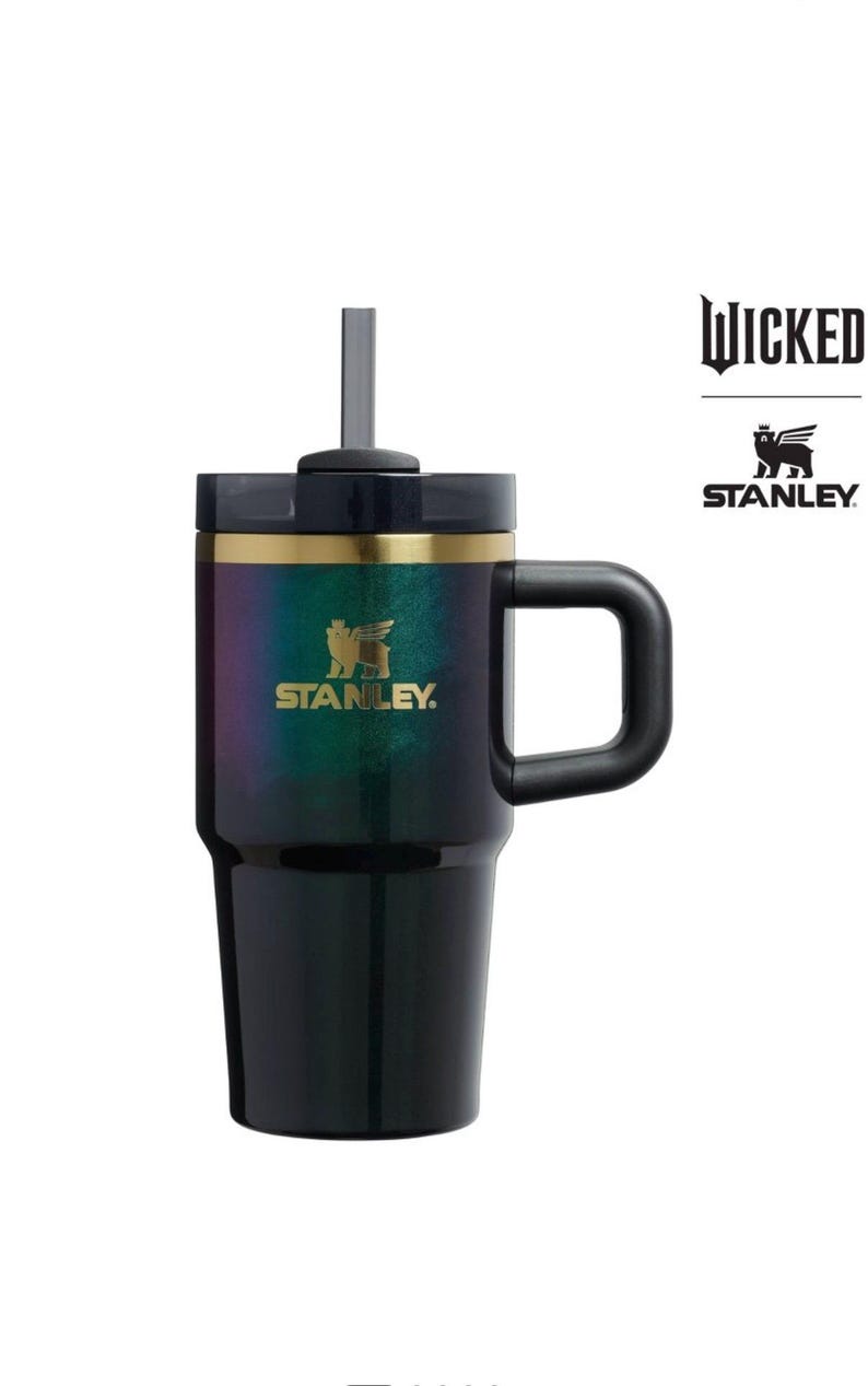 Op de afbeelding: Zwarte en iriserende Stanley-beker met een handvat en een rietje. De beker heeft een gouden band en het Stanley-logo. Het woord "WICKED" en het Stanley-logo staan aan de rechterkant van de beker.