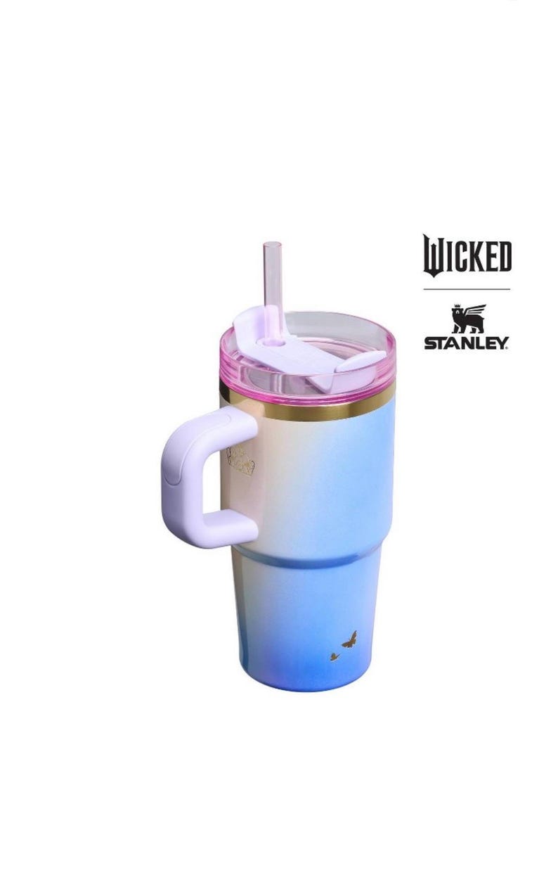 Op de afbeelding: Een Stanley-beker met een blauw-witte gradi&euml;nt, een roze deksel en een handvat. Op de beker staat het woord "WICKED" en het Stanley-logo. Twee kleine vogels zijn op de bodem van de beker gedrukt.
