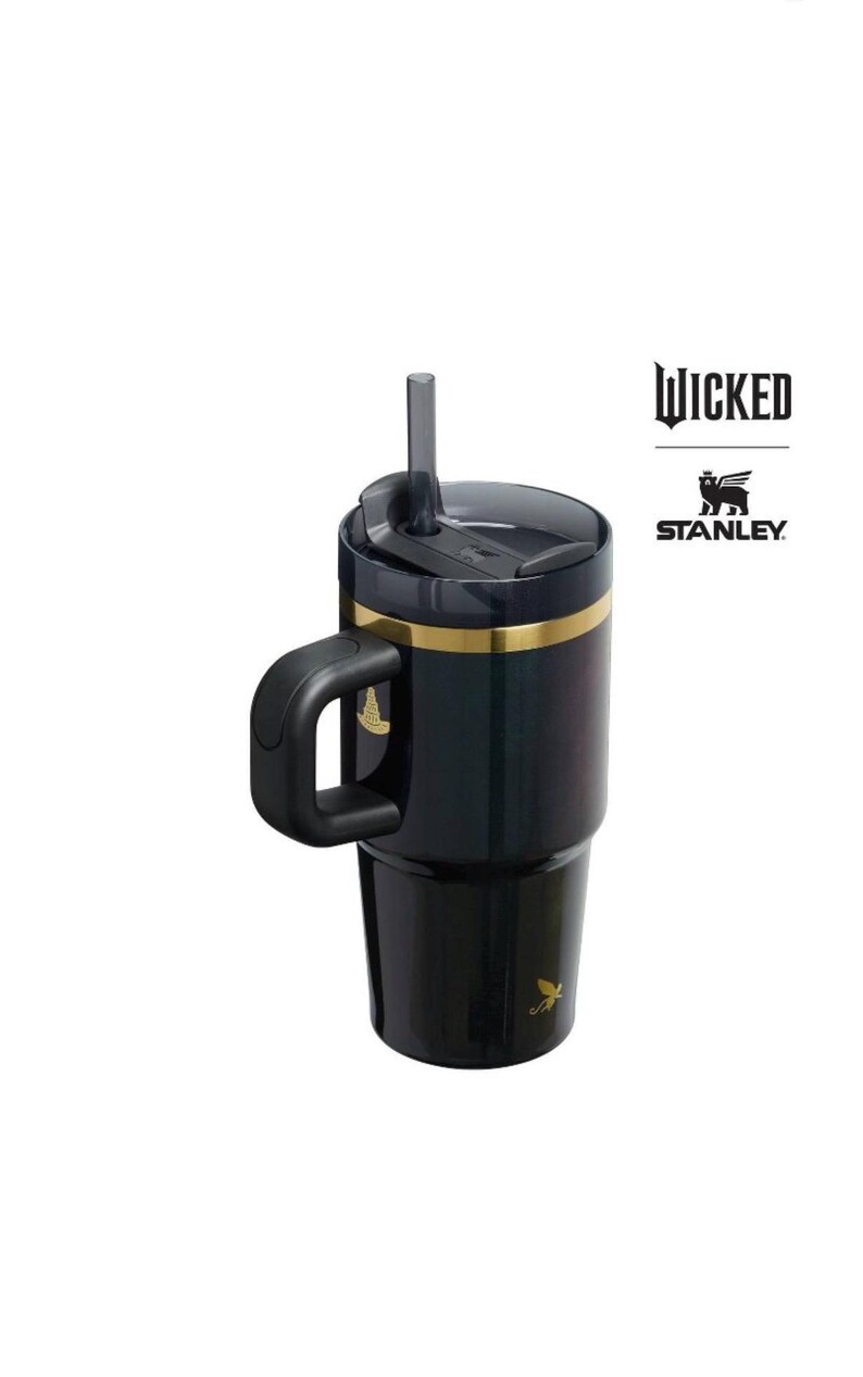 Op de afbeelding: Zwarte en gouden ge&iuml;soleerde beker met een handvat en een rietje. Op de beker staat het woord "WICKED" gedrukt, samen met het Stanley-logo. Een gouden accentband loopt rond de bovenkant van de beker.