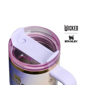 Op de afbeelding: Een Stanley reismok met een lichtpaarse deksel en handvat, en een gouden rand. De mok heeft een gradi&euml;nt afwerking, die overloopt van wit naar lichtblauw en paars. Het woord "WICKED" en het Stanley-logo zijn zichtbaar.