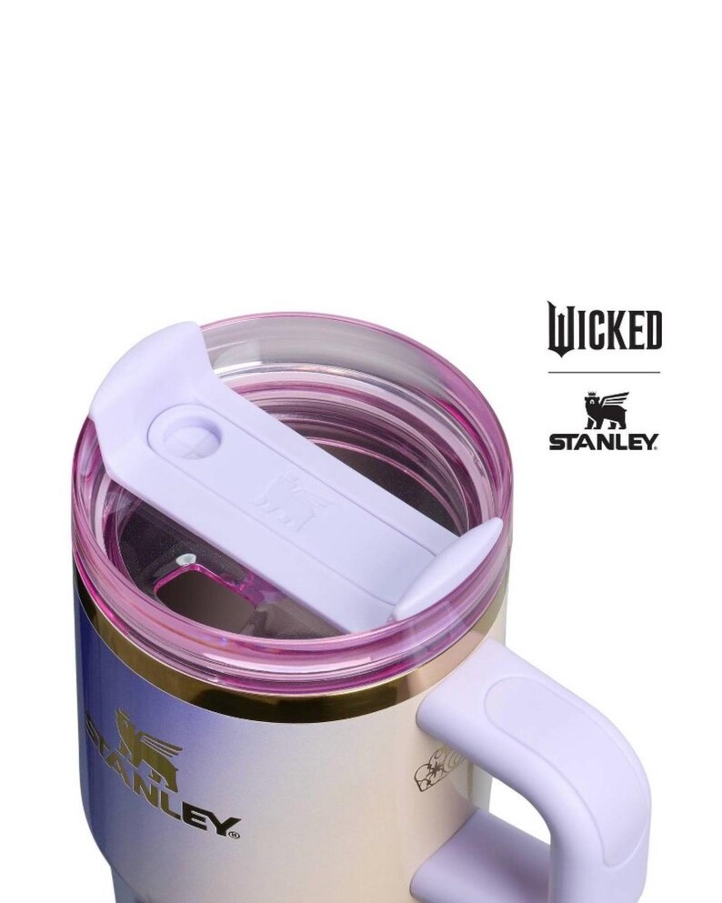 Op de afbeelding: Een Stanley reismok met een lichtpaarse deksel en handvat, en een gouden rand. De mok heeft een gradi&euml;nt afwerking, die overloopt van wit naar lichtblauw en paars. Het woord "WICKED" en het Stanley-logo zijn zichtbaar.