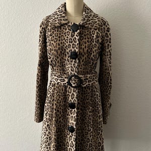 May include: A brown and black leopard print coat with a black belt and black buttons. The coat has a collar and long sleeves.